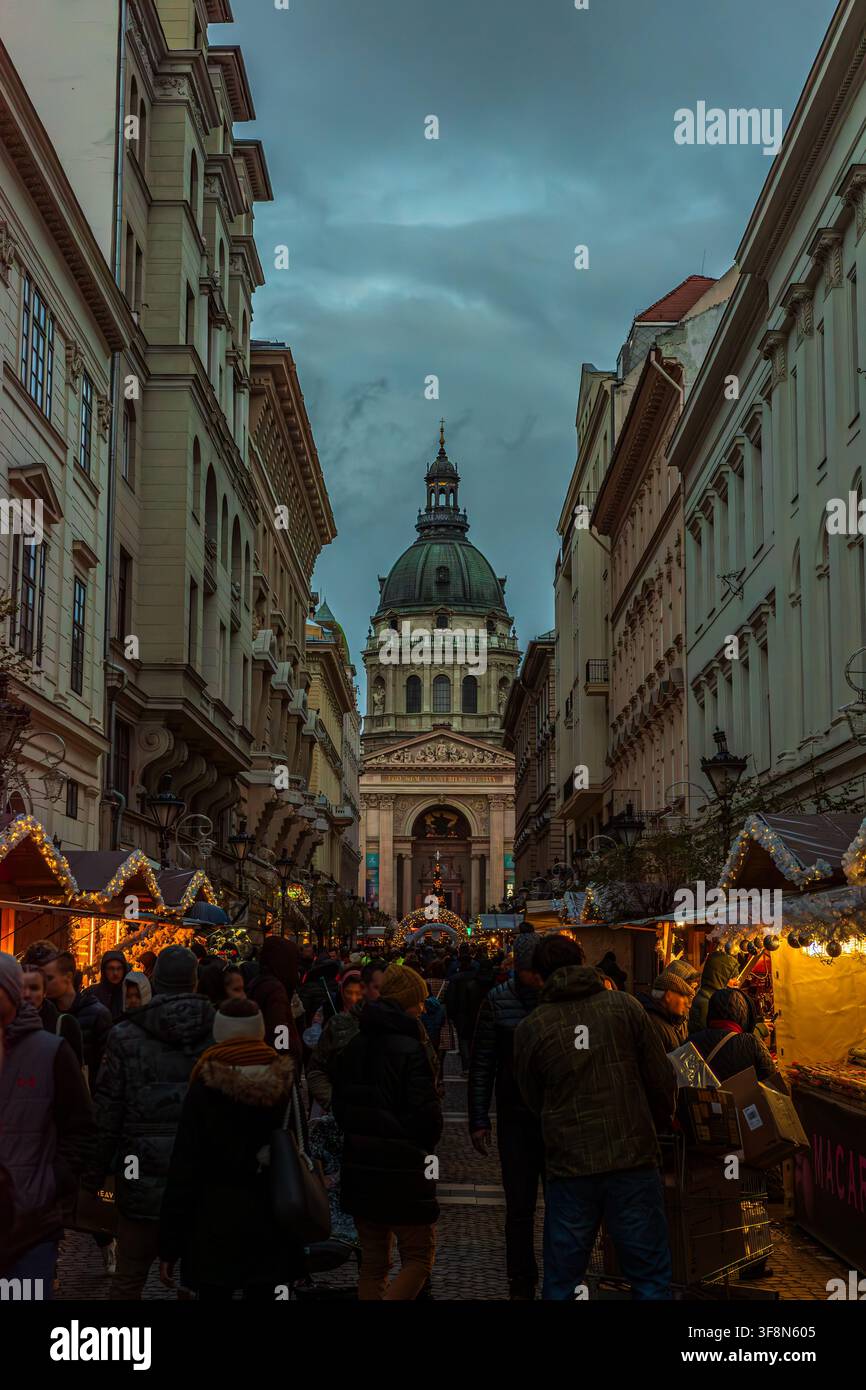 Vertikale Stadtschaftsfotografie eines geschäftigen Weihnachtsmarktes vor der St. Stephans-Basilika in Budapest, Ungarn. Das Bild zeigt einen schmalen Fußgängerbereich Stockfoto