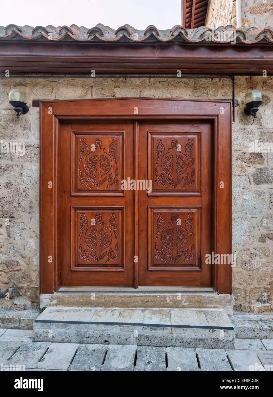 Eine kunstvolle traditionelle Holztür mit Granatapfel-Schnitzereien an einem alten Steinhaus im historischen Kaleici-Bezirk von Antalya, Türkei Stockfoto