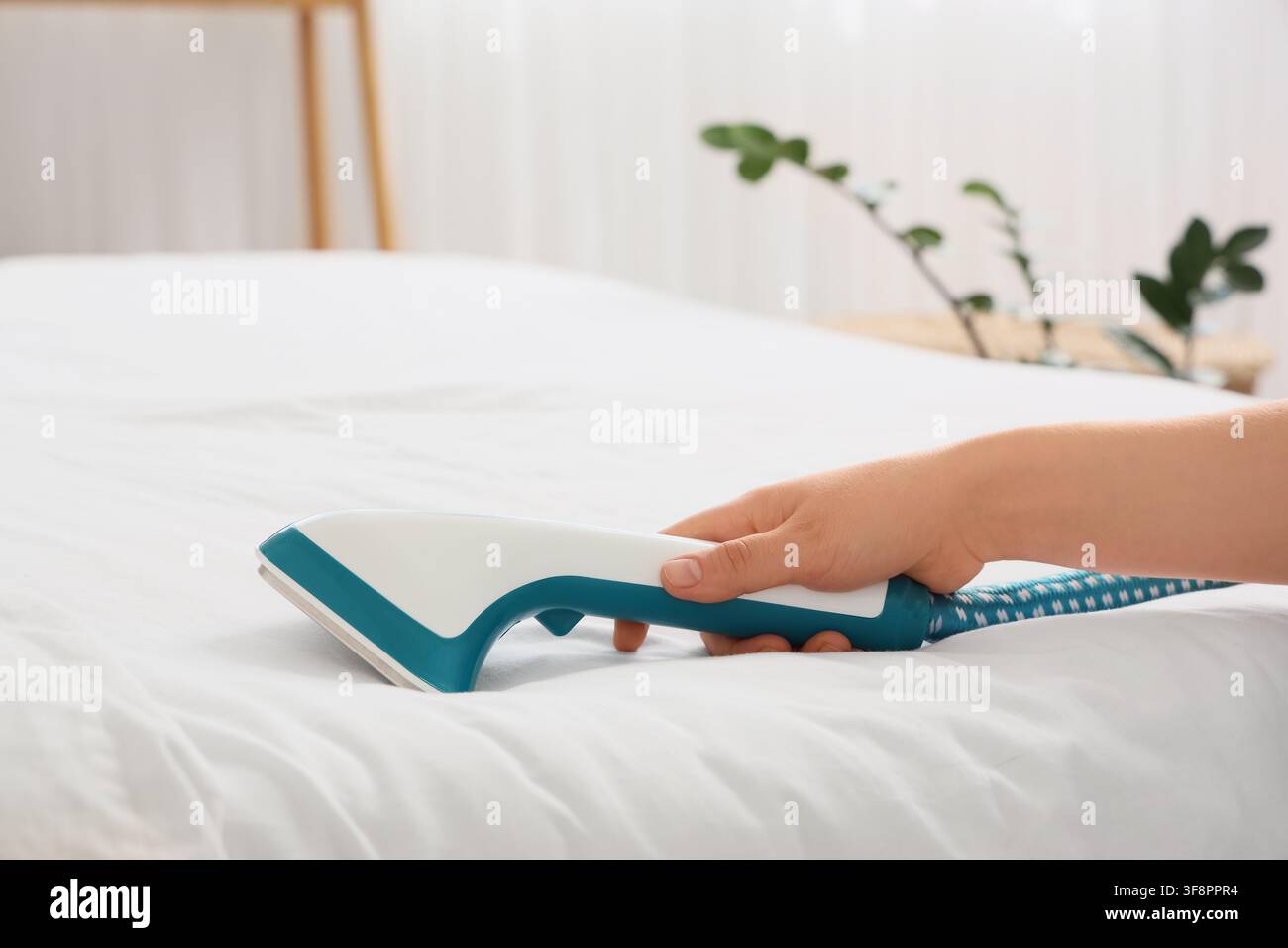 Hand, die einen modernen Stoffrasierer hält, der Flusen von weißen Bettlaken entfernt, Haushaltsarbeiten und Textilpflege Stockfoto