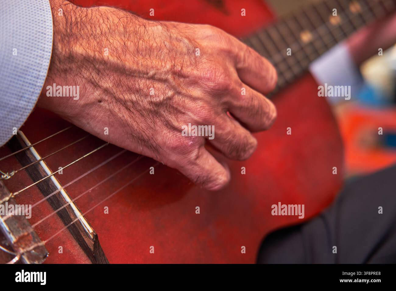 Männerhand zupft Nylonsaiten auf einer roten Akustikgitarre während eines Auftritts Stockfoto
