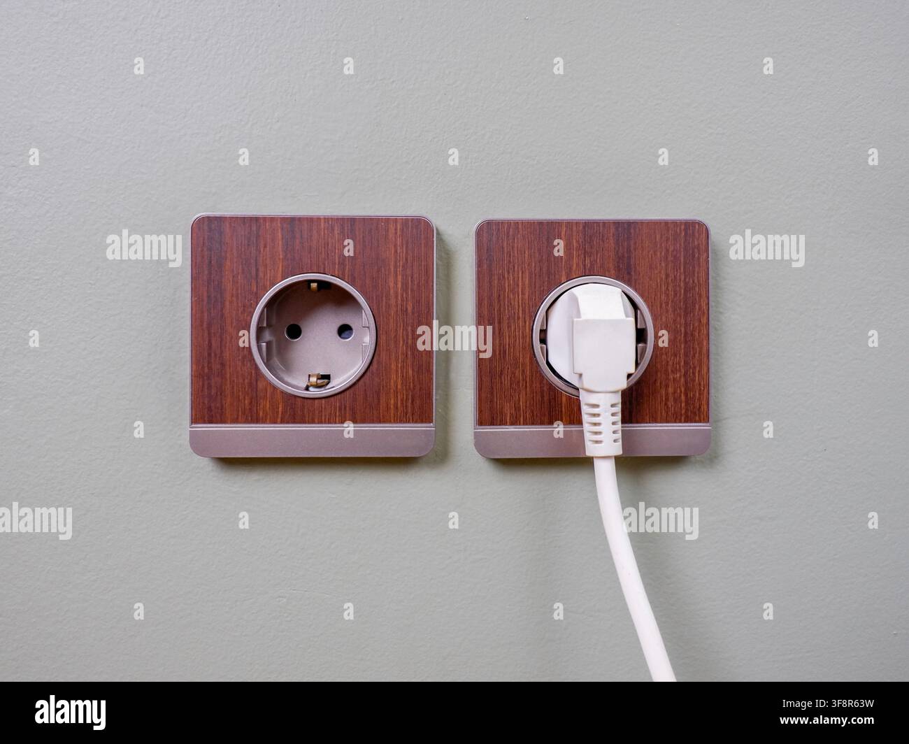 Zwei Typ-F-Steckdosen nebeneinander an einer hellgrünen Wand montiert. Ein weißer Stromstecker ist an der rechten Steckdose angeschlossen. Stockfoto
