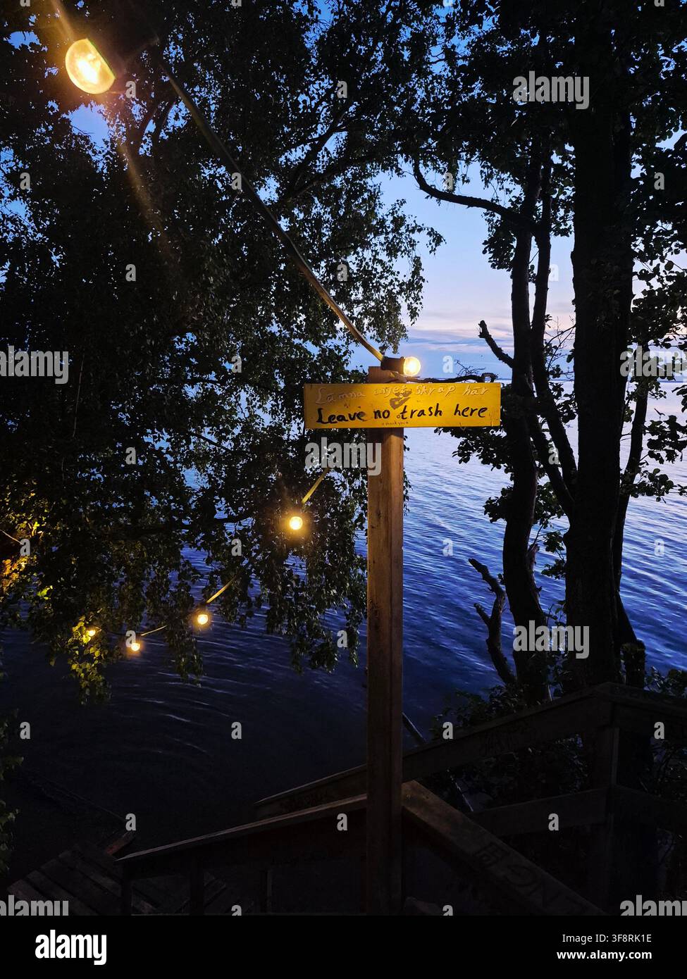 Holzschild „Leave Only Footprints“ neben einem friedlichen See, umgeben von Bäumen im Abendlicht Stockfoto