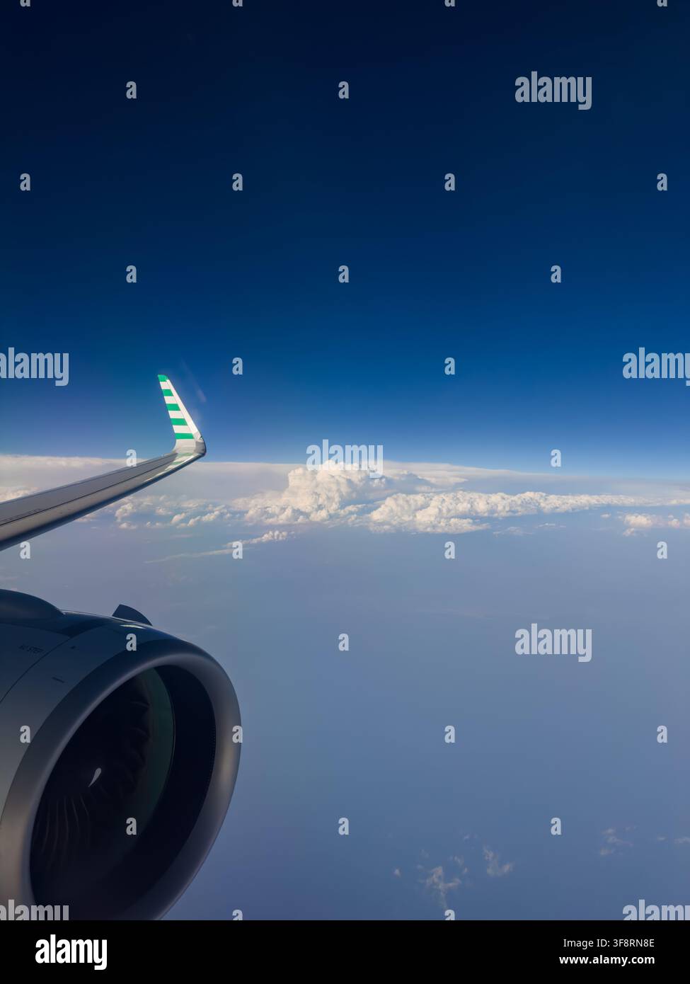 Blick aus dem Flugzeugfenster, der ein Triebwerk und einen Flügel über einem weiten blauen Ozean und einer Wolkenschicht zeigt Stockfoto