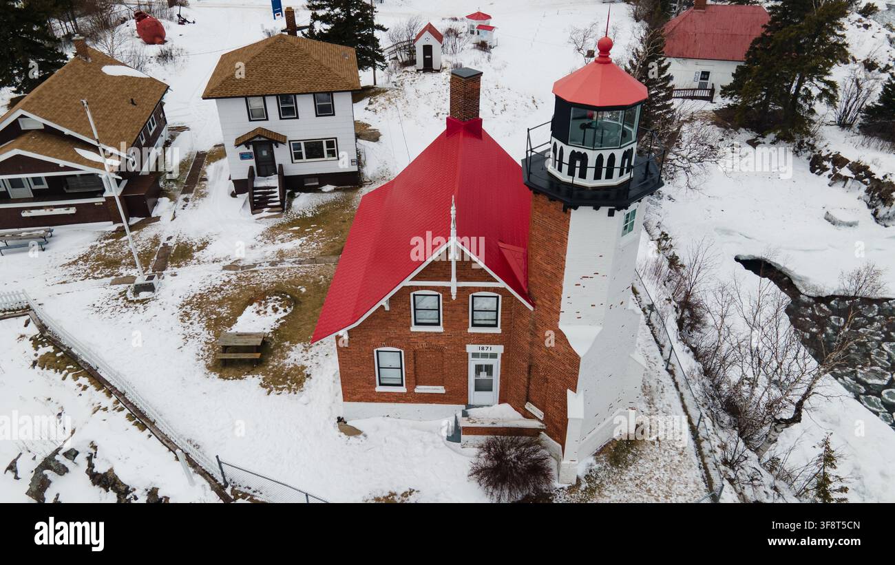 Luftaufnahme des historischen Eagle-Harbor-Leuchtturms mit seinem markanten roten Dach, umgeben von schneebedeckten Grundstücken und Gebäuden in Eagle Harbor, Mi Stockfoto