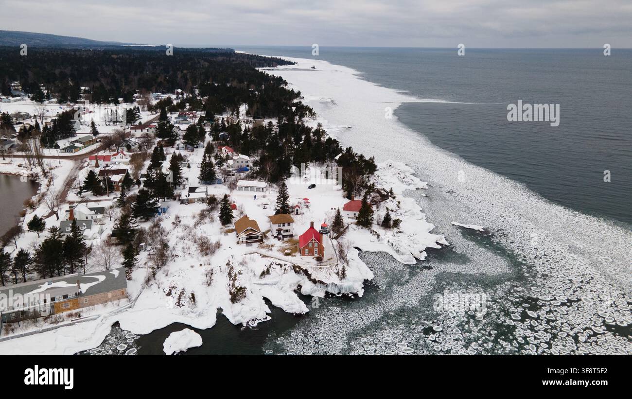 Luftaufnahme des Eagle Harbor Leuchtturms, umgeben von einer schneebedeckten Landschaft und eisigem Wasser des Lake Superior in Eagle Harbor, Michigan, Vereinigte Staaten. Stockfoto