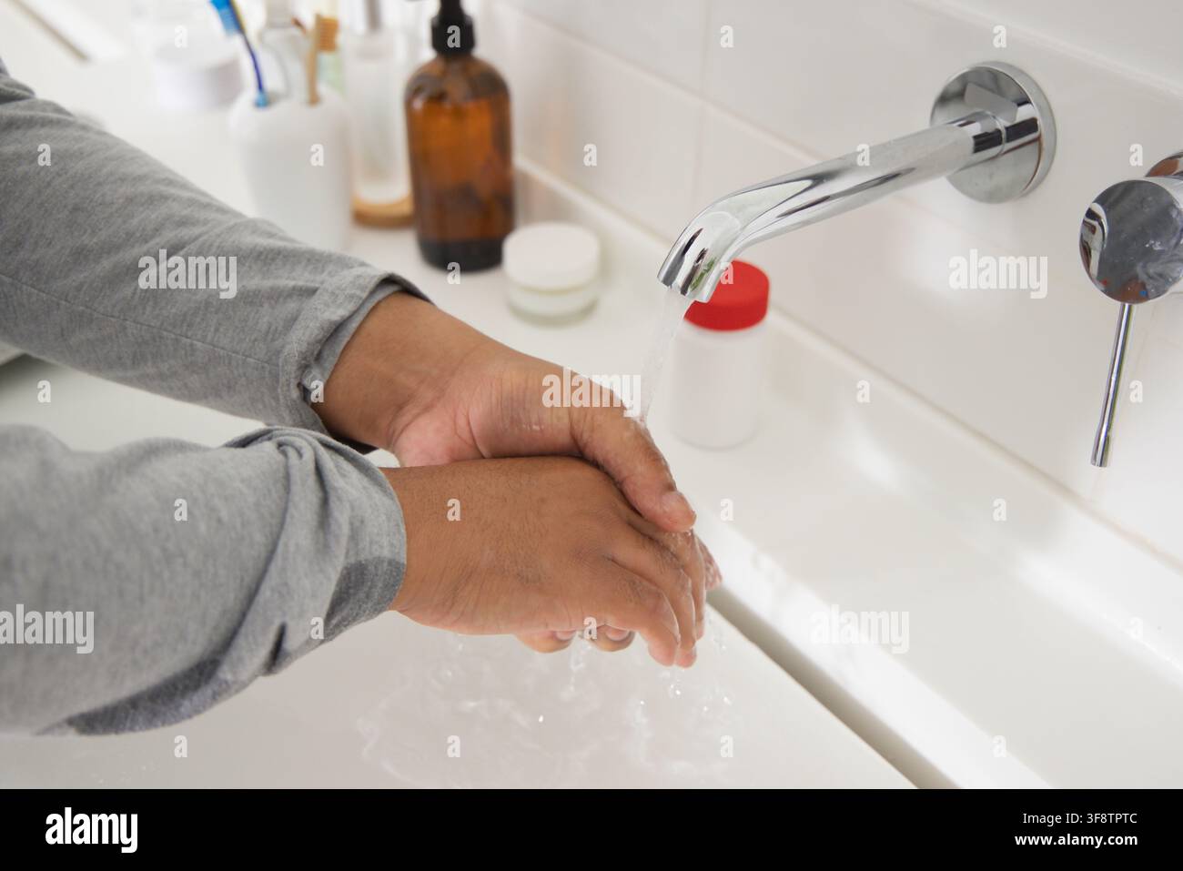 Erwachener afrikanischer Mann wäscht sich die Hände und reibt die Handflächen unter einem an der Wand montierten Chromwasserhahn am Waschbecken Stockfoto