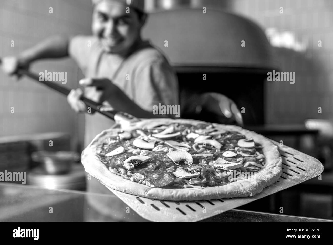 Koch stellt die Pizza in den heißen Ofen zum Backen. Der Koch bereitet Pizza mit einer Schaufel in den Händen vor. Schwarz und Weiß Stockfoto