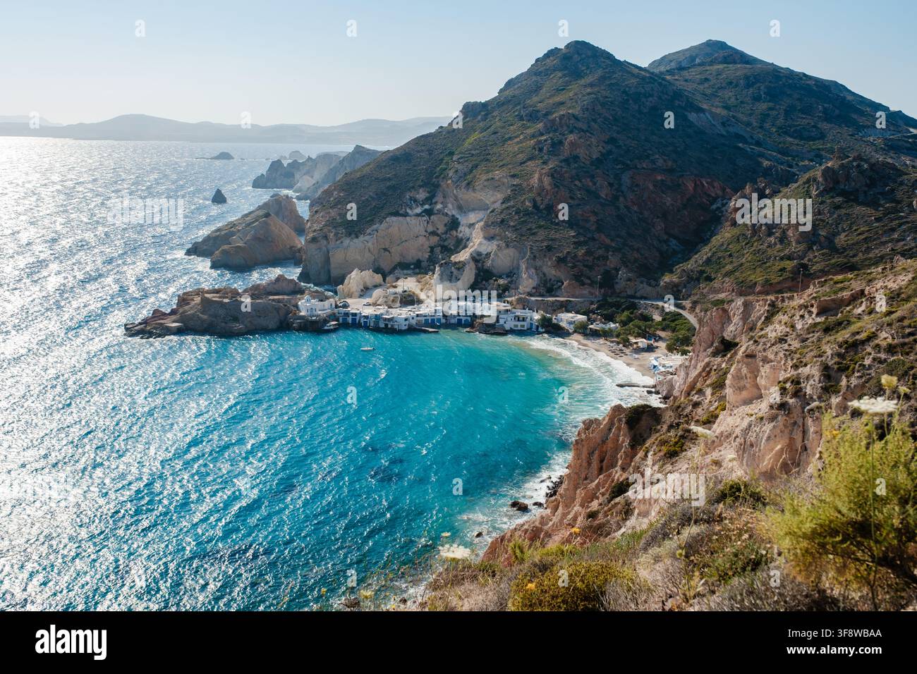 Glitzernde türkisfarbene Gewässer umarmen die Ufer von Firopotamos in Milos, Griechenland. Eingebettet zwischen felsigen Klippen heben charmante Gebäude die natürliche Schönheit hervor Stockfoto
