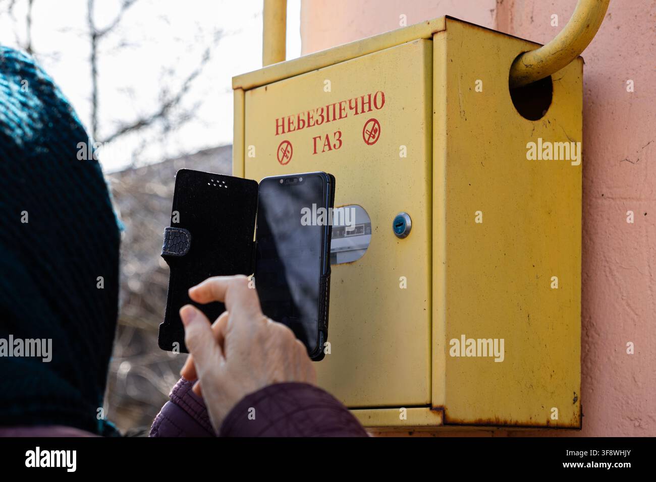 Nahaufnahme einer älteren Person, die mit einem Smartphone Messwerte von einem wandmontierten Gaszähler aufnimmt, um die wesentliche Instandhaltung der Haushaltsversorgung hervorzuheben Stockfoto