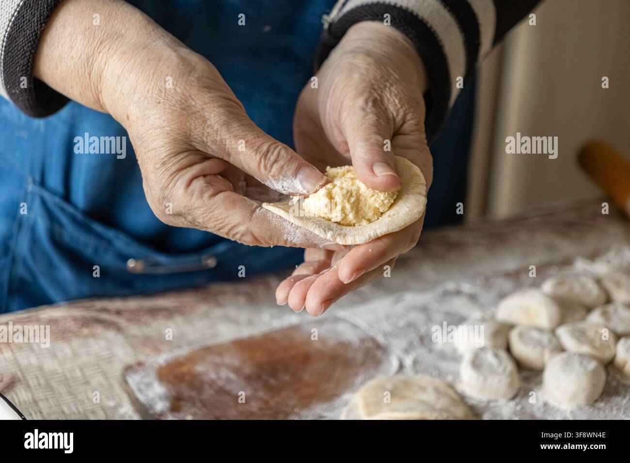 Geschickte faltige Hände bereiten hausgemachte Teiglinge zu, die mit cremiger Füllung auf einem mehligen Holzbrett gestopft werden, und fangen die Wärme der traditionellen Kochkunst ein Stockfoto