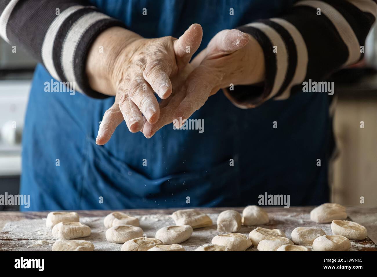 Ein älterer Koch formt Stücke von rohem Teig für hausgemachte Knödel auf einem mehligen Tisch, was die Hingabe und das Handwerk verdeutlicht, die mit der Zubereitung von frischem f verbunden sind Stockfoto