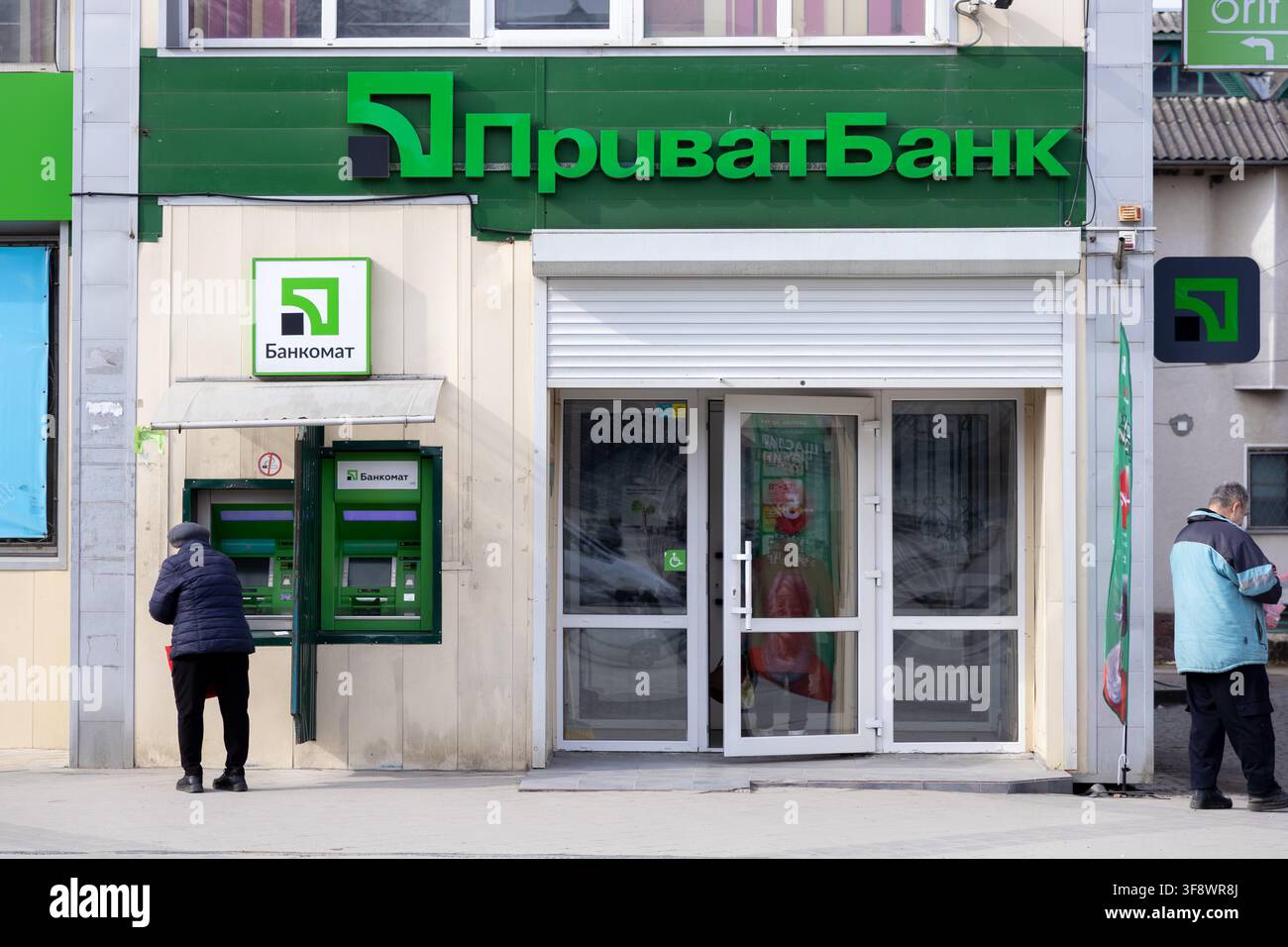 Horodok, Ukraine - 23. März 2026: Fassade des PrivatBank-Gebäudes mit einem Kunden an einem Außen-ATM für Bargeldabhebungen während eines Zusammenbruchs Stockfoto