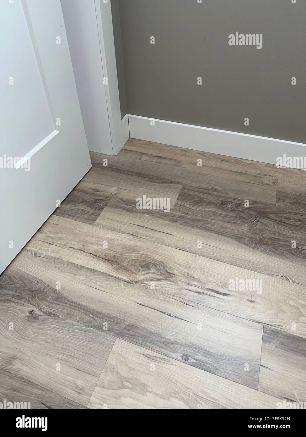 Innenecke zeigt Luxus-Vinylplanken in Holzoptik, die auf weiße Sockelleisten und einen Türrahmen in einer modernen Sanierung treffen. Stockfoto