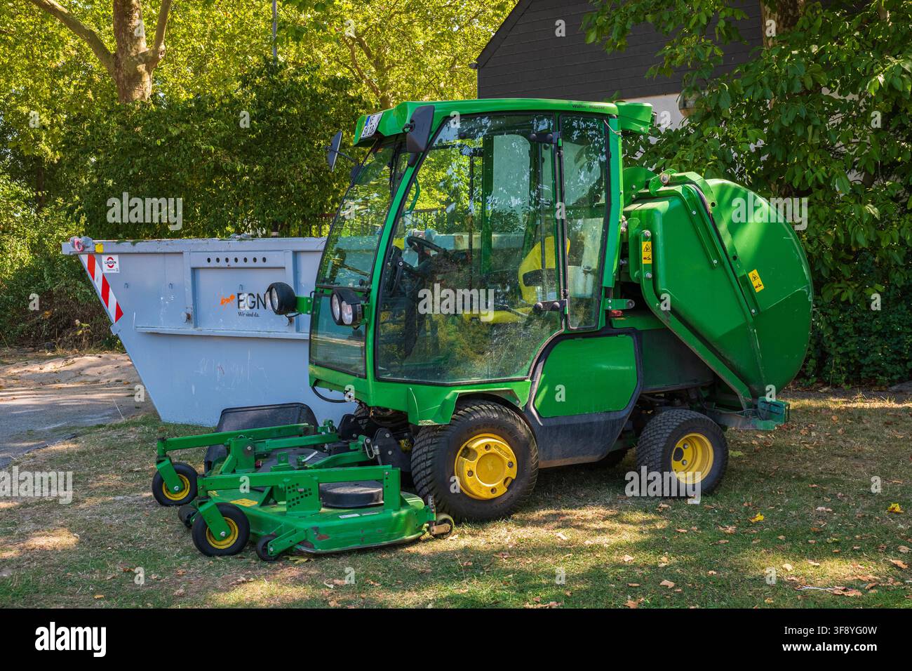 Grüner kommunaler Nutzfahrzeugtraktor mit Rasenmäherdeck und Abfallbehälter, geparkt in einem Park, professionelle Landschaftsgestaltungs- und Grundstückspflegeausrüstung Stockfoto