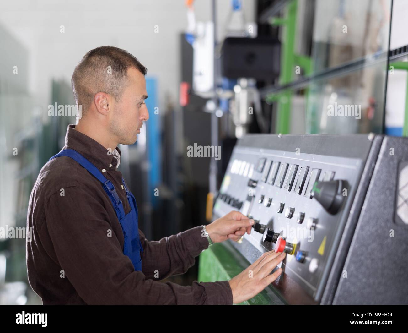 Professioneller Bediener, der an der Maschinensteuertafel im Glaswerk arbeitet Stockfoto