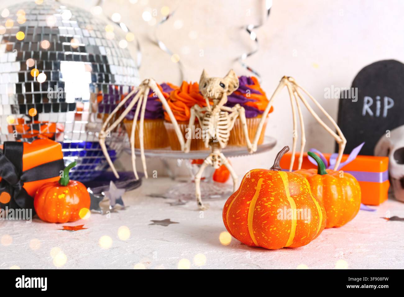 Halloween-Party-Dekorationen mit Fledermaus-Skelett, Kürbissen, Cupcakes und Diskokugel auf einem festlichen Tisch Stockfoto