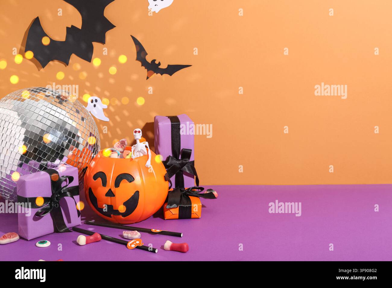 Halloween-Party-Dekorationen mit Diskokugel-Kürbis-Süßigkeiten-Eimer-Skelett- und Geister-Ausschneidefiguren auf orangefarbenem und lila Hintergrund Stockfoto