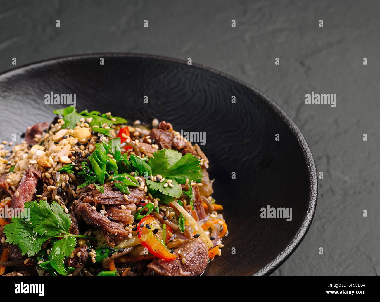 Soba-Nudeln und gebratenes Rindfleisch mit frischem Koriander, Erdnüssen und Gemüse in einer schwarzen Schüssel Stockfoto