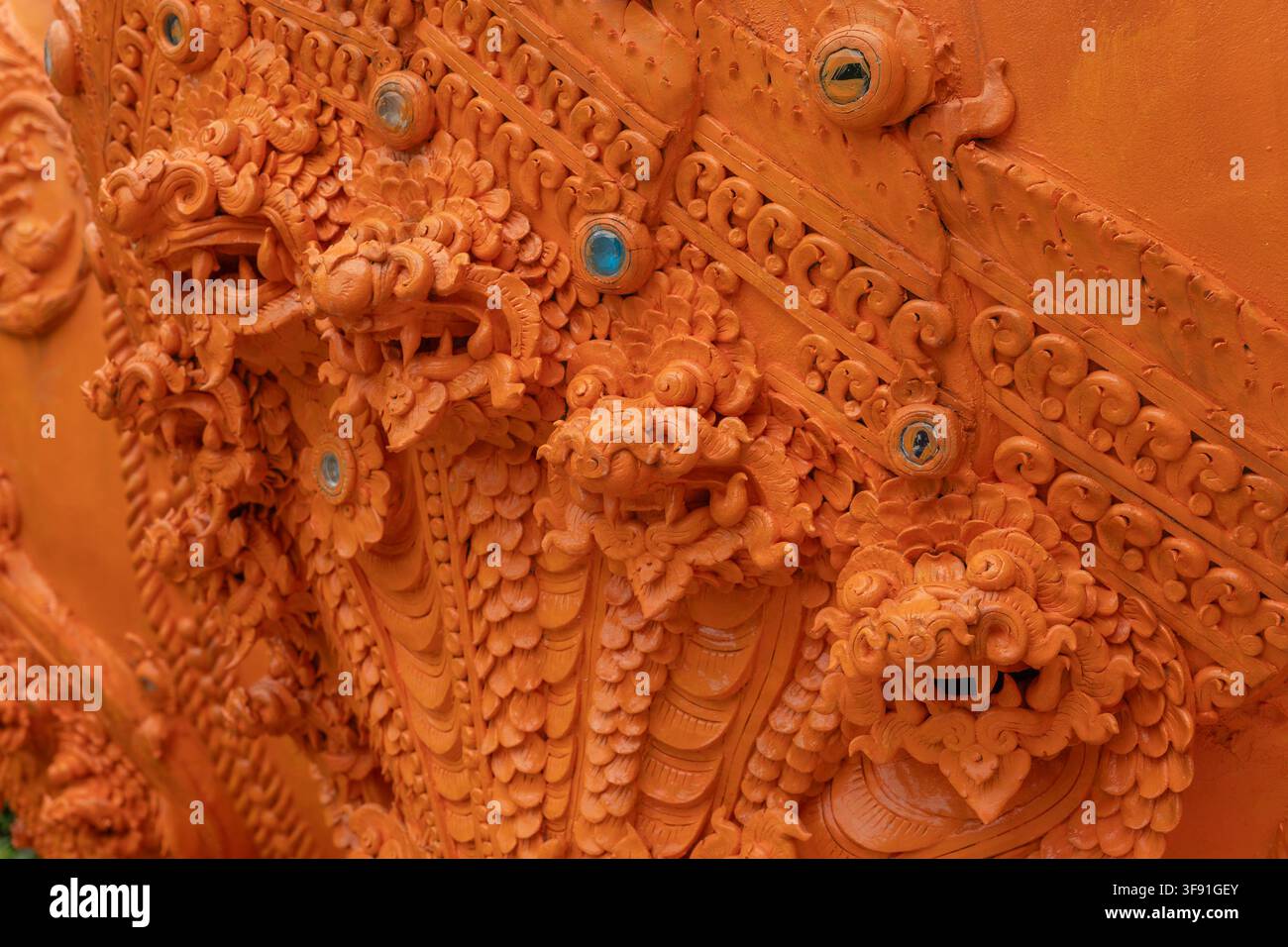 Nahaufnahme eines aufwendig geschnitzten Orangen-Tempelwandornaments mit mehreren mythischen Kreaturen, Blumenmotiven und aufwendigen Dekorationselementen Stockfoto