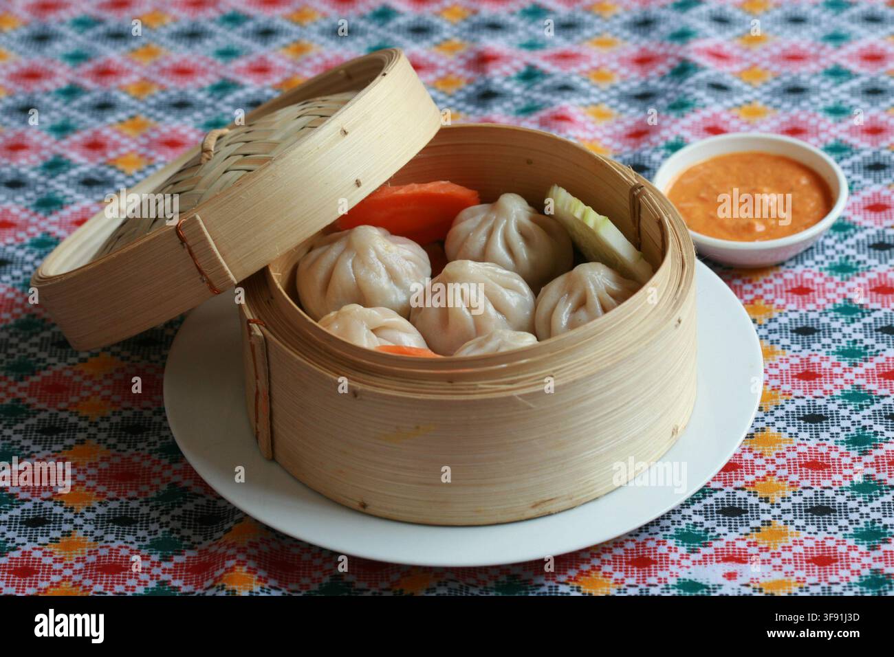 Frisch gedämpfte Momo-Teigtaschen, serviert in einem traditionellen Bambusdampfgarer mit einer kleinen Schüssel scharfer Dip-Sauce. Stockfoto