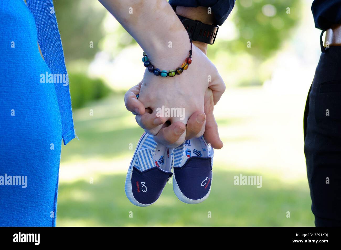 Schwangere Eltern halten kleine Babyschuhe, während sie im Freien stehen und die Vorfreude auf das neue Leben feiern Stockfoto