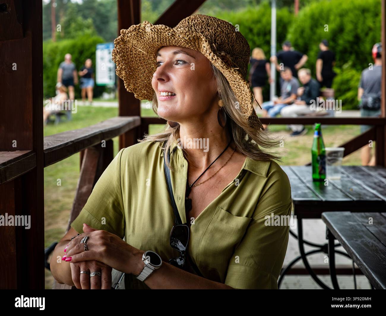 Frau mit Strohhut entspannt sich an einem Außenstand während eines Sommerfestes Stockfoto