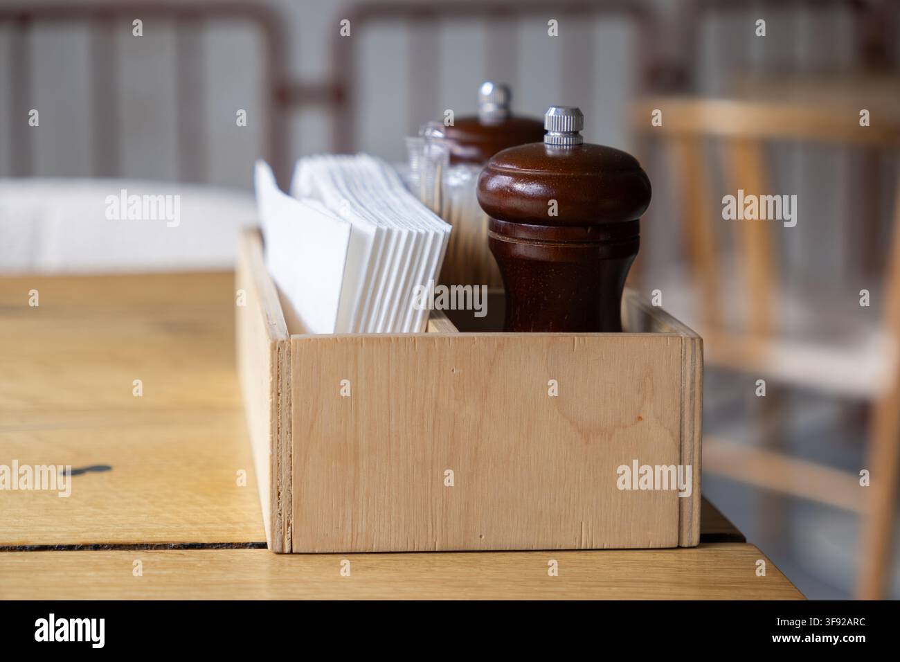 Der rustikale Gewürz-Organisator mit weißen Servietten und brauner Holzgewürzmühle ruht auf einem Tisch und bietet den Gästen wesentliche Servicegegenstände in einem warmen Stockfoto