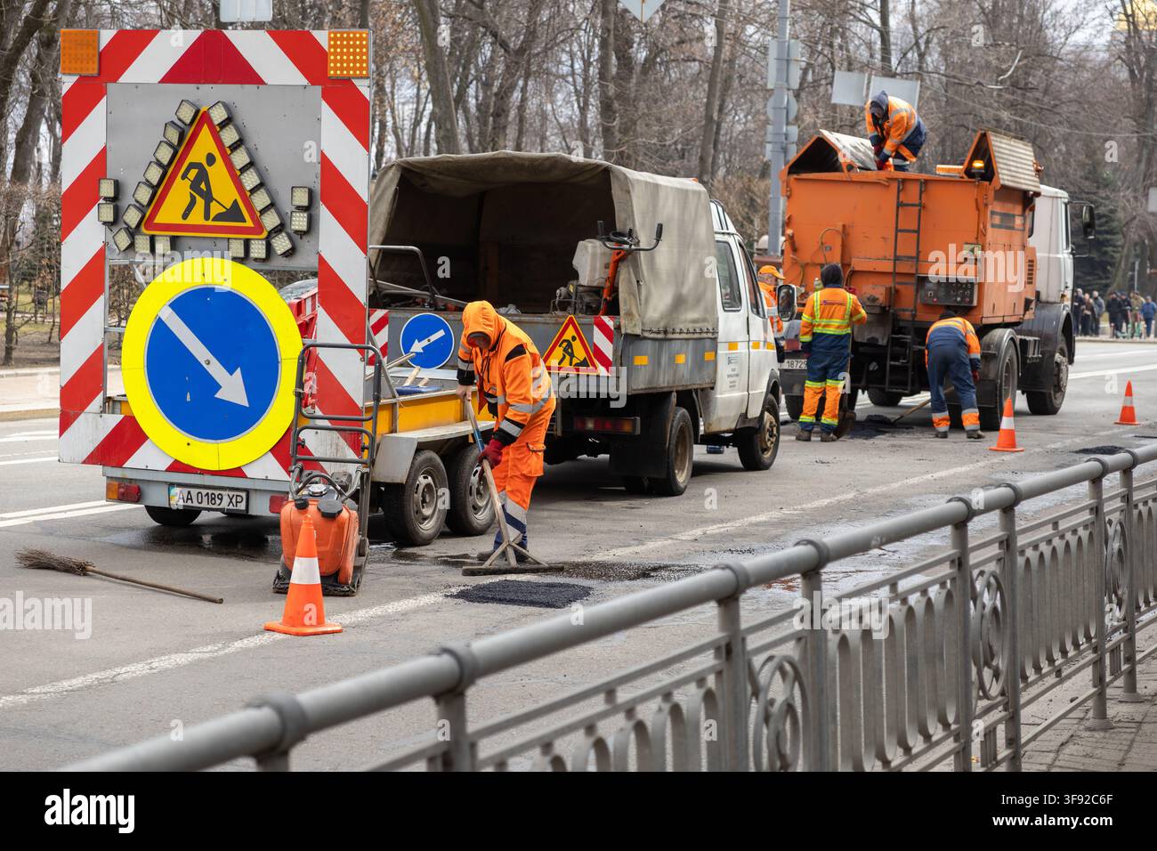 Kiew, Ukraine – 22. März 2026: Arbeiter in Warnkleidung reparieren Schlaglöcher auf der Straße mit spezialisiertem Gerät und warnenden Verkehrsmarkern Stockfoto
