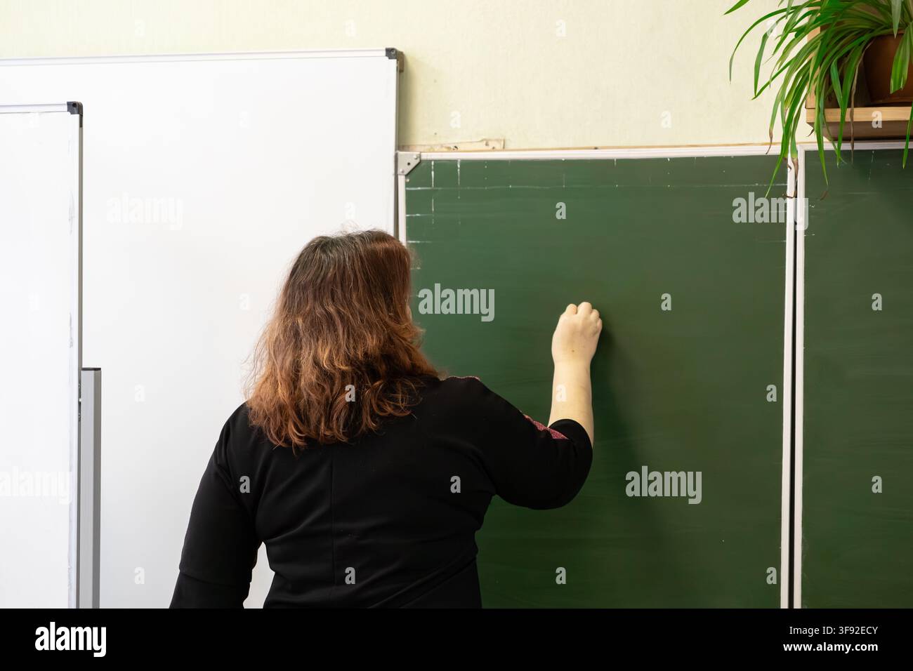 Pädagoge steht vor einer Klassenzimmer-Tafel und verwendet Kreide, um Lektionen mit Schülern zu teilen, was berufliche Hingabe und aktives Lernen in einer p darstellt Stockfoto
