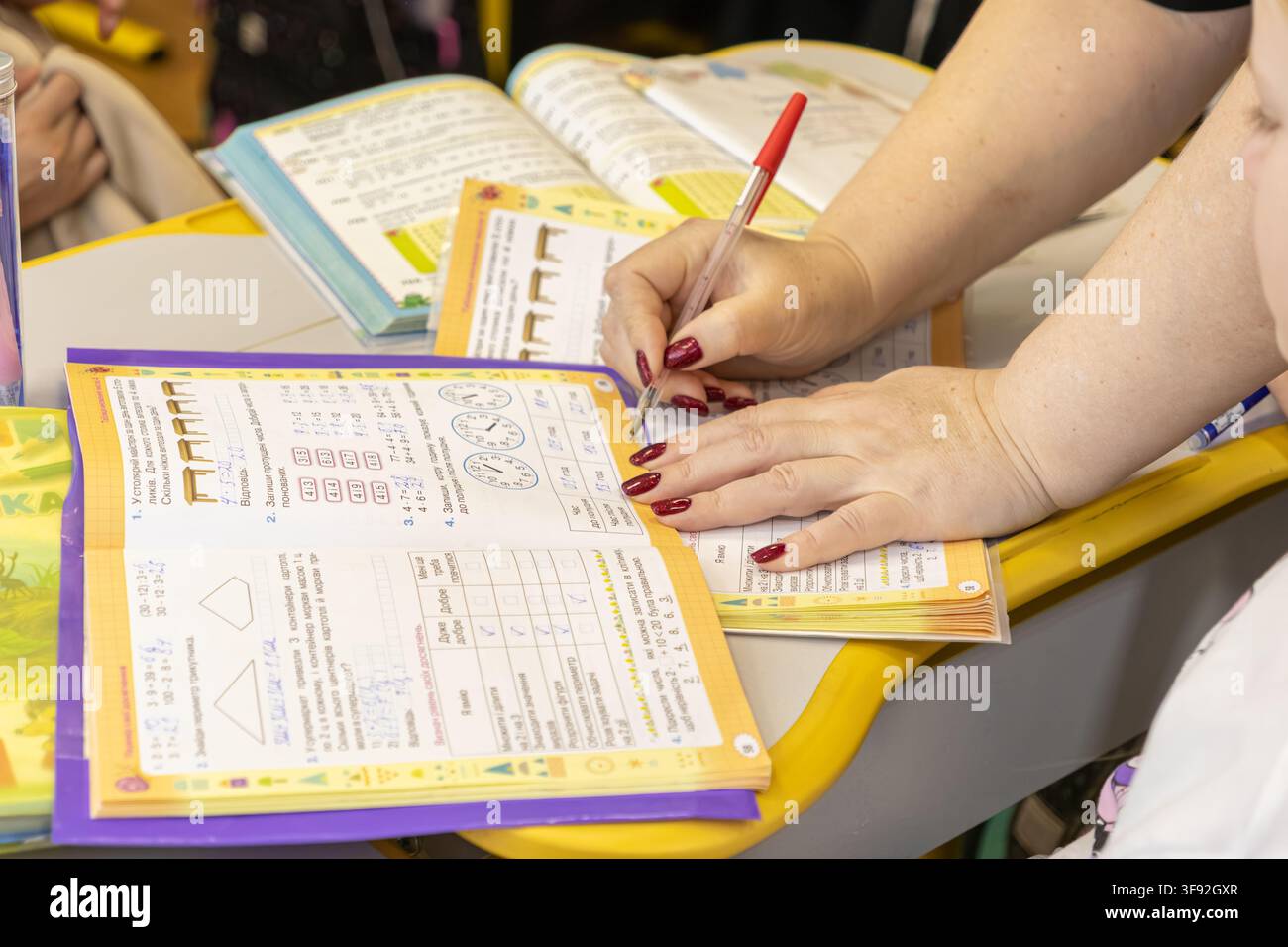 Kiew, Ukraine – 20. März 2026: Ein Lehrer verwendet einen roten Stift, um Seiten in den Arbeitsheften der Schüler auf einem Holzschreibtisch zu markieren, um engagierte Pädagogen widerzuspiegeln Stockfoto