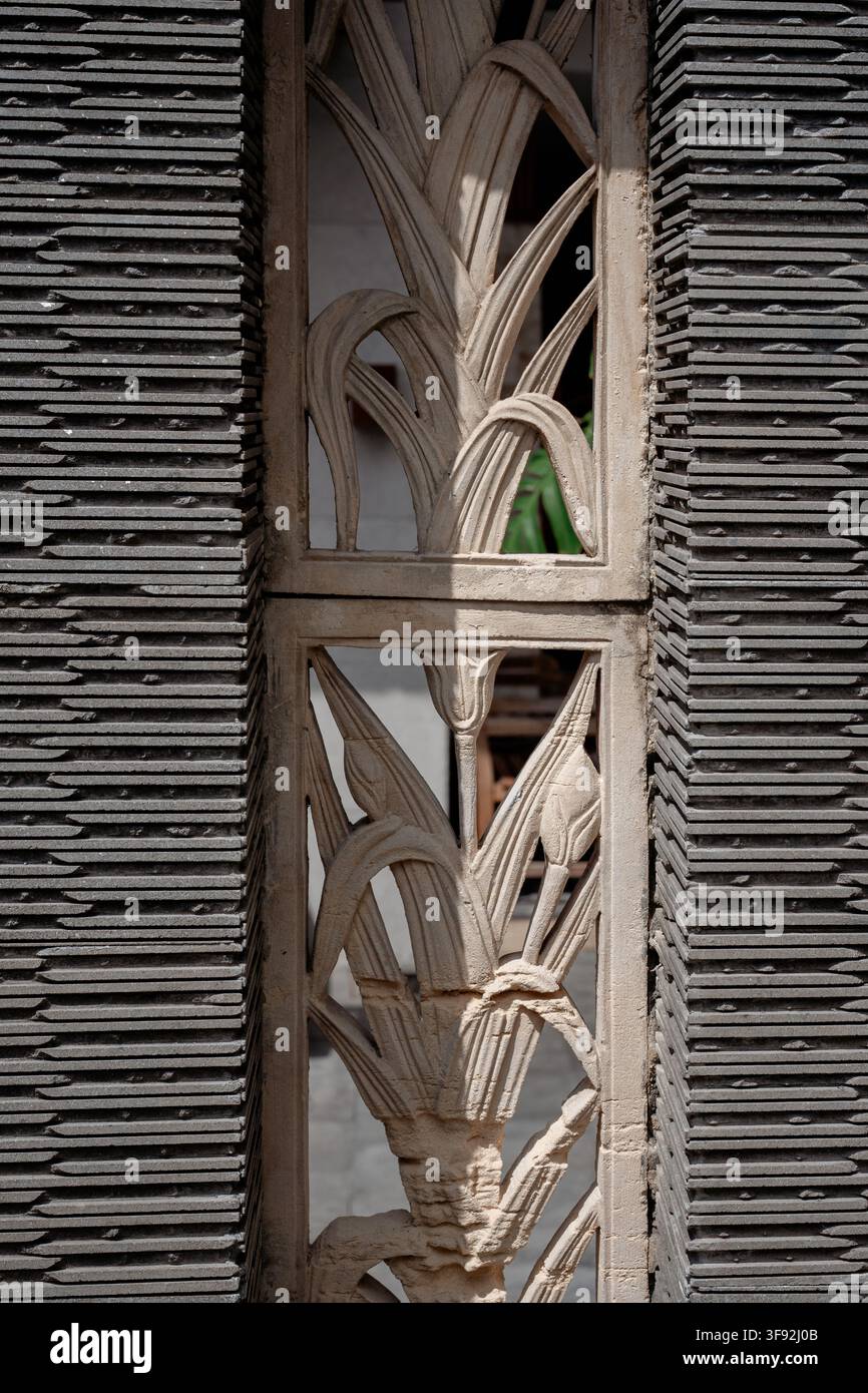 Architektonisches Detailbild mit einer zentralen Steinreliefdarstellung von Blattmotiven, flankiert von dunkelgrauen lamellierten oder gerillten Steinwandpaneelen. Stockfoto