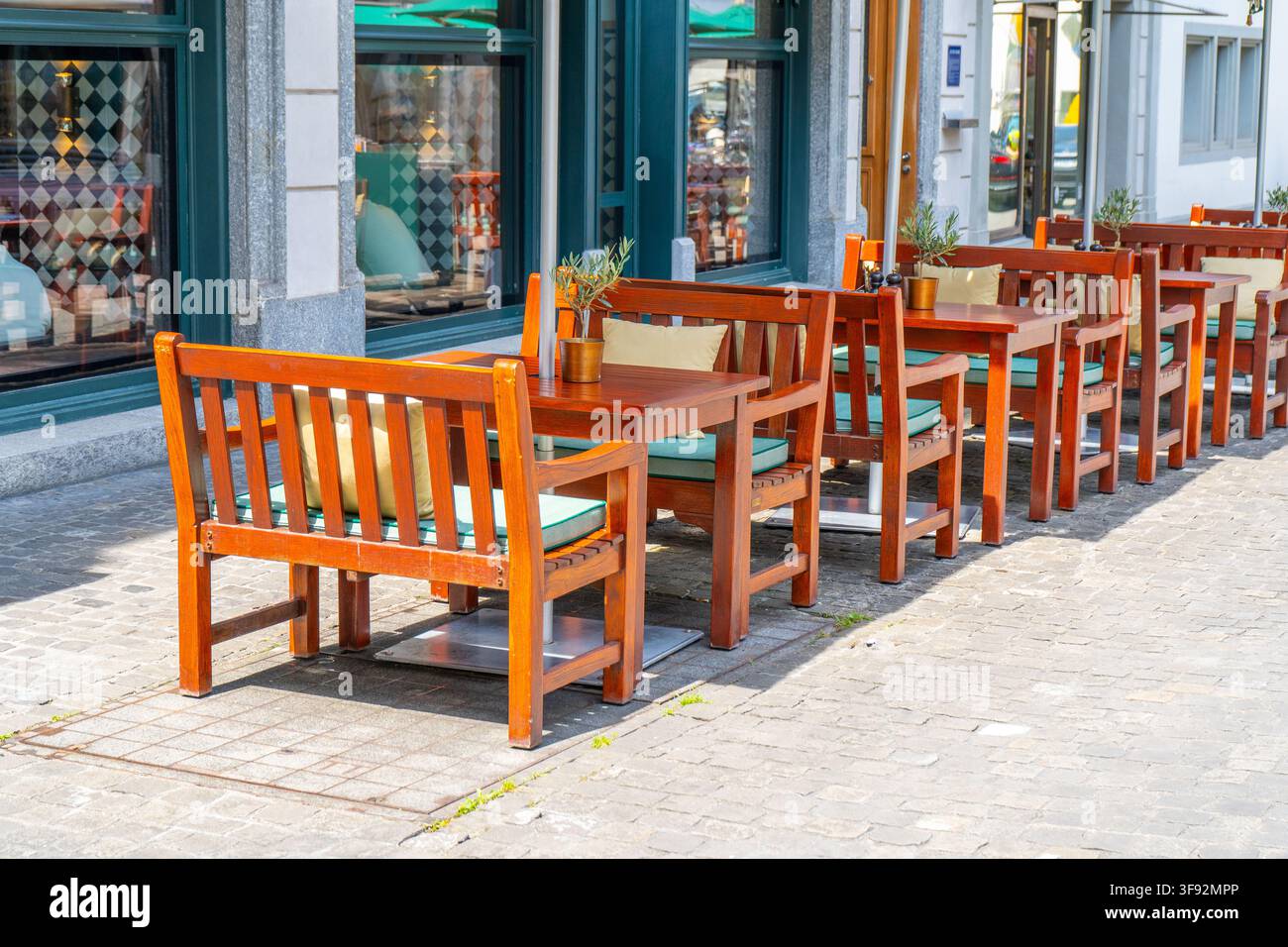 Holzstühle und Tische auf alter Straße vor gemütlicher europäischer Restaurantterrasse im Sommer. Stockfoto