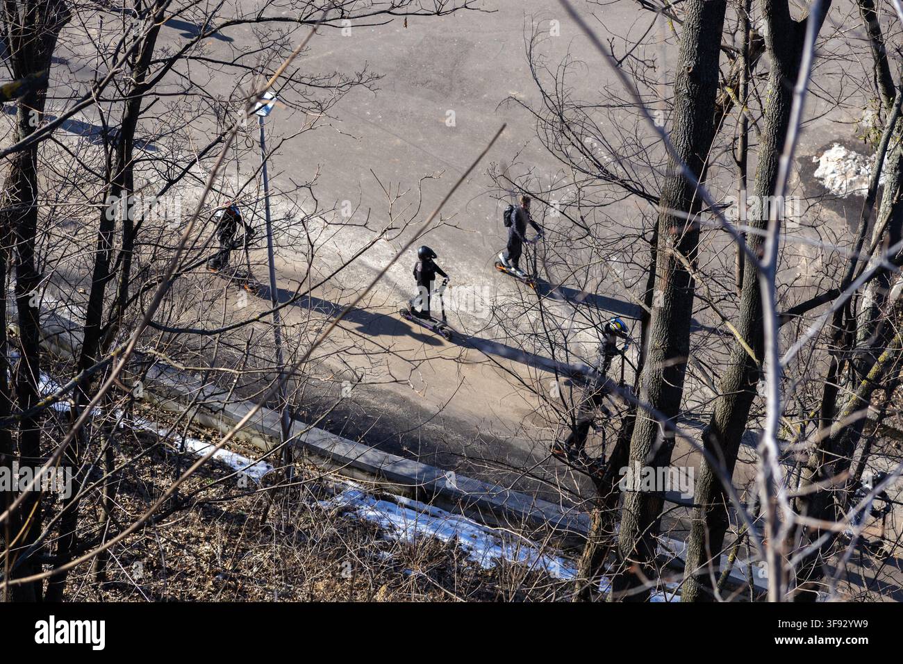 Personen, die auf modernen E-Scootern einen sonnenbeschienenen Parkweg entlangpendeln, was nachhaltigen Stadtverkehr und Freizeitaktivitäten im Freien hervorhebt Stockfoto