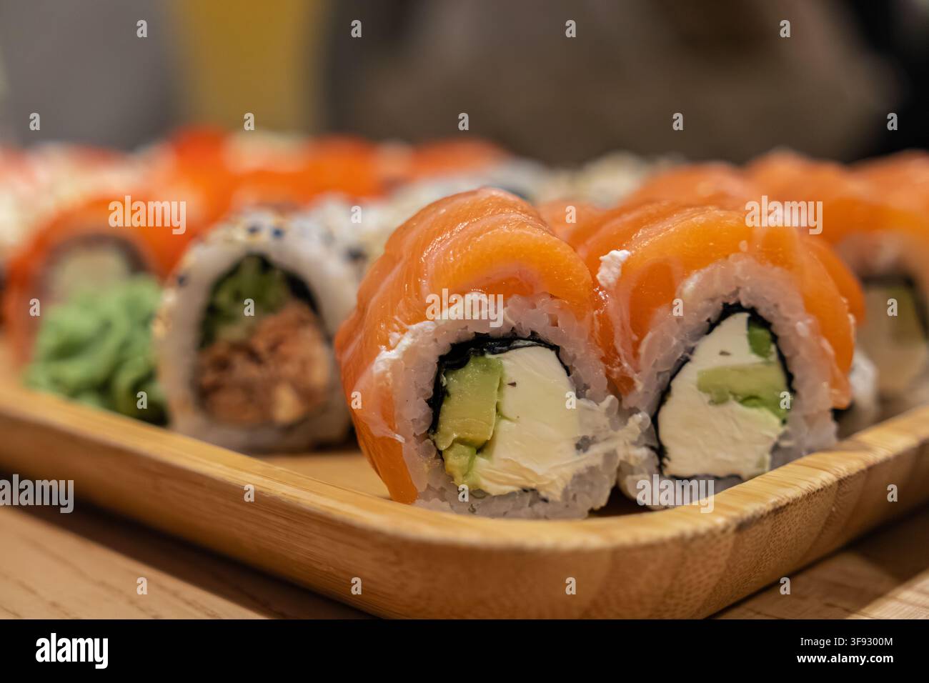Appetitlicher Philadelphia-Sushi-Maki, ordentlich auf einem Holztablett angeordnet, betont die lebendige Textur von Fisch und cremigen Füllungen für gehobene Culi Stockfoto