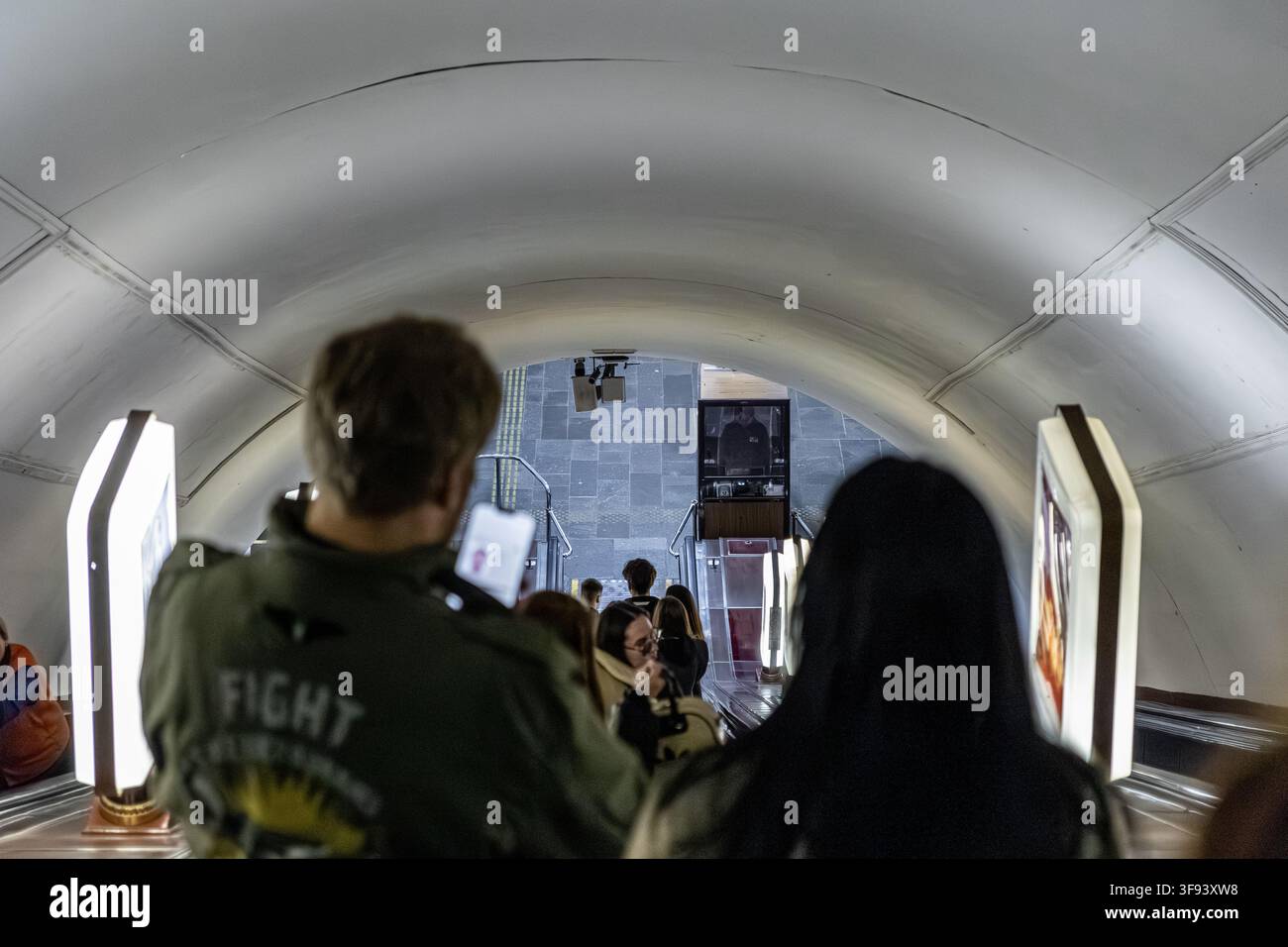 Kiew, Ukraine – 15. März 2026: Pendler steigen eine lange Rolltreppe in einer tunnelartigen U-Bahn-Station hinab, was den ständigen Strom von Menschen betont und d Stockfoto