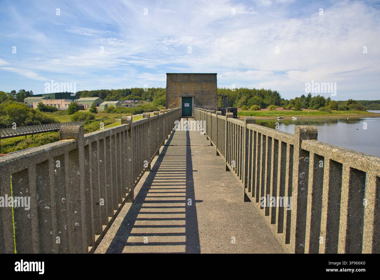 Erhöhter Gehweg oben auf dem Llyn Cefni-Staudamm, der zum zentralen Kontrollturm in Anglesey, Wales, führt. Stockfoto