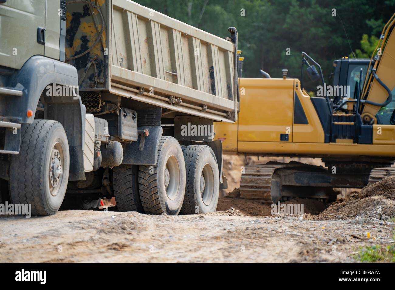 Schwerlastkippwagen neben Kettenbagger, der auf der Baustelle Tiefbau- und Erdbewegungsarbeiten durchführt Stockfoto