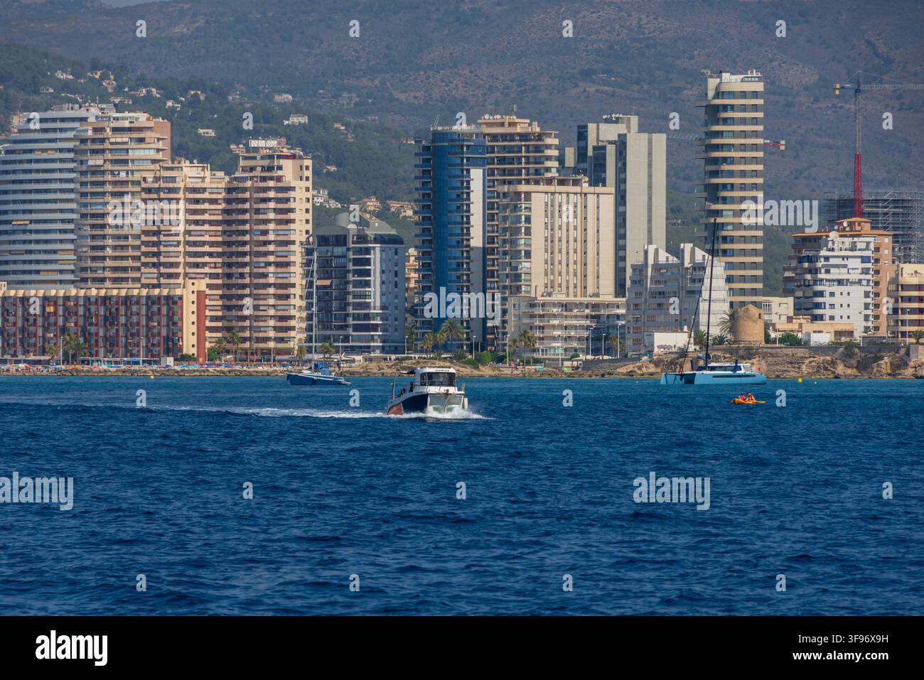 Calp, Spanien - 11. Juli 2027: Blick auf die Küsten skyline mit modernen Hochhäusern, einem Motorboot, das auf dem blauen Mittelmeer kreuzt, und klarem Stockfoto