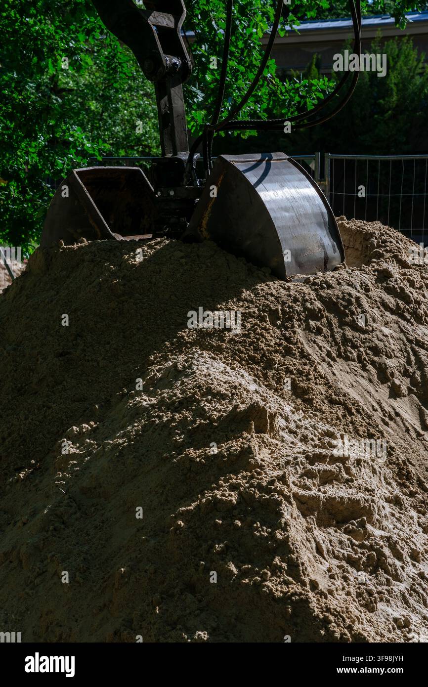 Nahaufnahme eines Baggerlöffels, der in einem Sandhaufen auf einer Baustelle ruht. Generische Erdbewegungs- und Ausgrabungsszene. Stockfoto