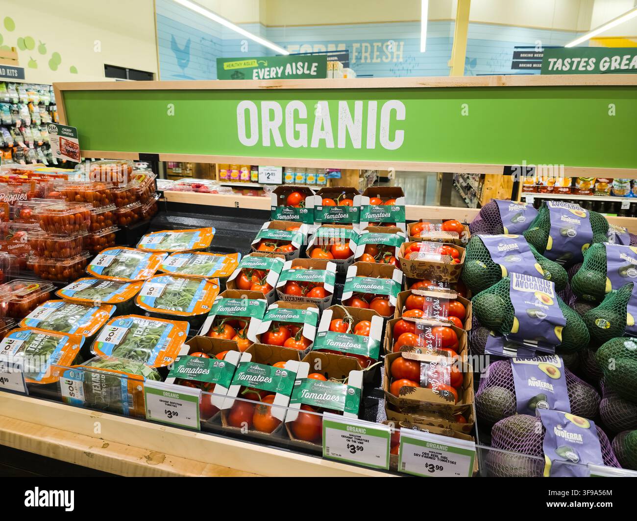 ADDISSON, TX, USA - 26. JULI 2026: Ein Supermarktgang zeigt eine Vielzahl von Bio-Produkten, darunter verpackte Tomaten und Avocados unter einer großen Stockfoto