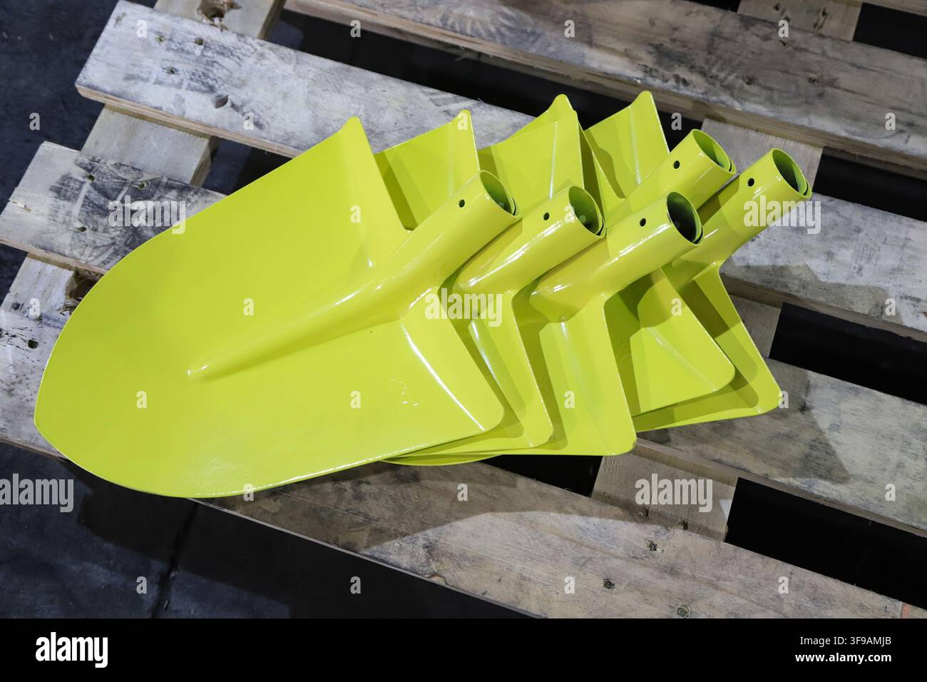 Mehrere lackierte hellgelbe Metallschaufeln sind ordentlich auf Holzpaletten platziert, mit einer glatten und glänzenden Lackierung, die den Zustand von fa Stockfoto