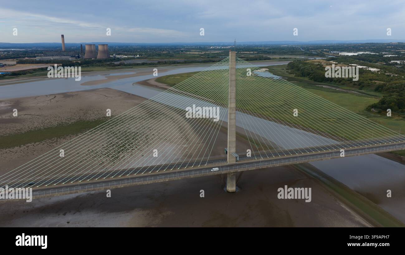 Luftbild der Mersey Gateway Bridge, die den Fluss Mersey überspannt, mit Schlickflächen und industriellen Kühltürmen in der Ferne in Runcorn, Vereinigtes Königreich Stockfoto