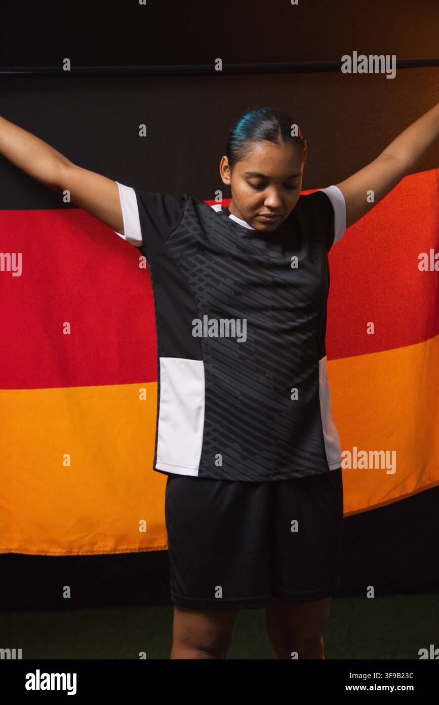 Female athlete standing holding black red gold fabric wearing black jersey and shorts in studio Stockfoto