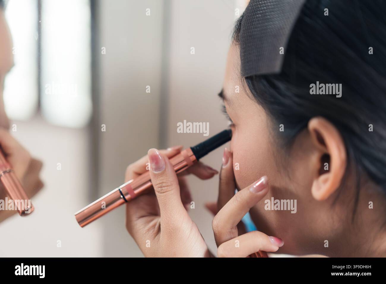 Nahaufnahme Porträt einer attraktiven asiatischen Frau, die sich bereit macht, Gesichtskosmetik aufträgt, Augenbrauen formt, Augenbrauen, Augenlinker vor dem Spiegel Stockfoto
