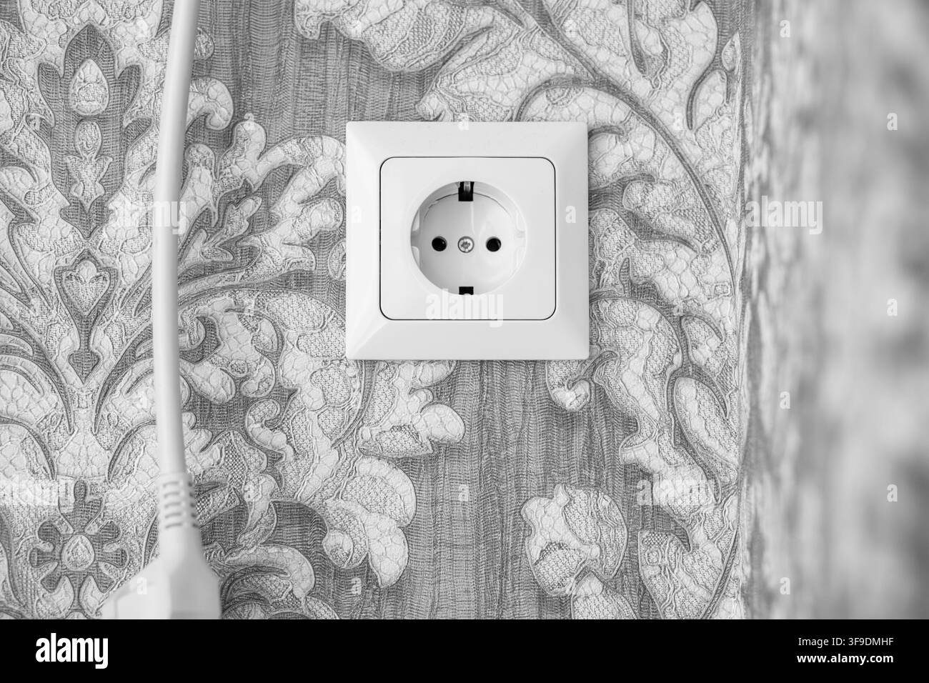 Elektrosteckdose mit weißem Stecker vor einem gemusterten Tapetenhintergrund in einer modernen Inneneinrichtung Stockfoto