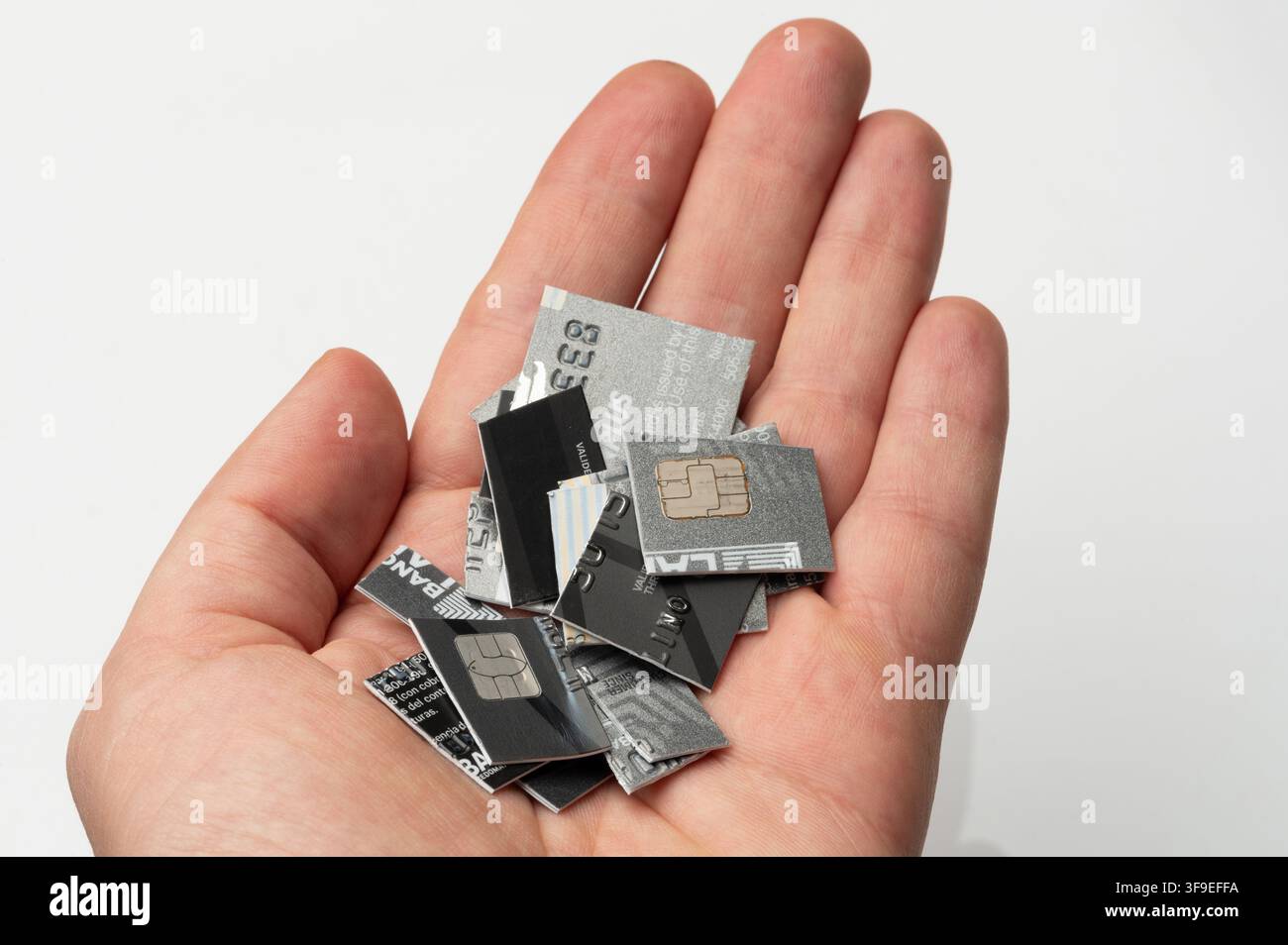 Eine Hand zeigt viele kleine Stücke geschnittener Kreditkarten auf einer weißen Oberfläche. Die Karten sind nicht mehr verwendbar. Stockfoto