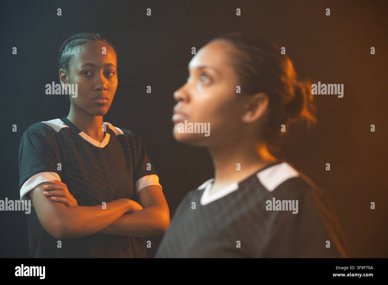 Fußballerinnen posieren in passenden schwarzen Sporttrikots mit weißem Rand unter Studiolicht Stockfoto