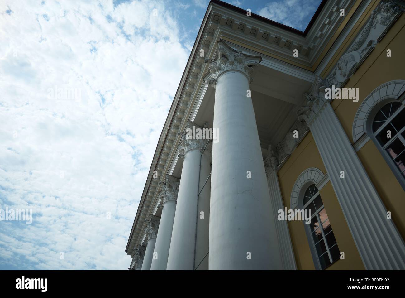 Niedrigwinkelansicht eines klassischen Gebäudes mit verzierten korinthischen Säulen, dekorativem Gebälk, geschnitzten Gesimsdetails und gelber Fassade unter bewölktem Himmel Stockfoto