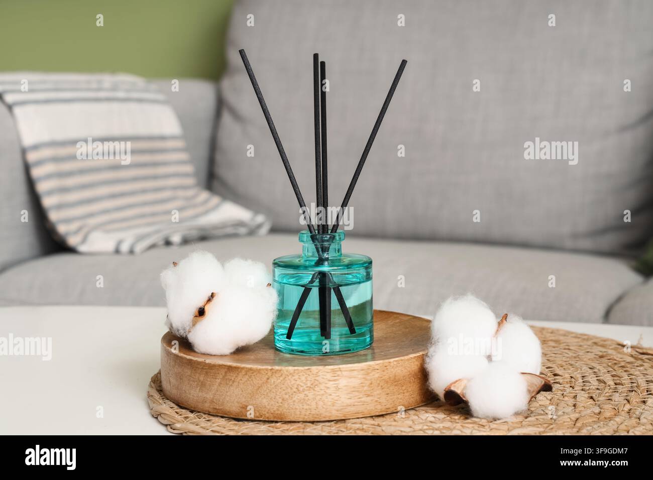 Schilf-Diffuser mit Baumwollblüten auf einem Holztray, Heimduft und Aromatherapie zur Entspannung, das Arrangement steht auf einem weißen Tisch in einem Wohnraum Stockfoto