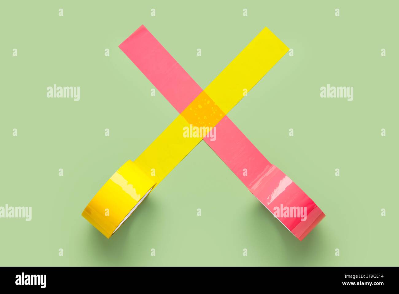 Gelb- und pinkfarbenes Klebeband, das eine X-Form auf einem pastellgrünen Hintergrund bildet, abstrakte Kunst und Design, die hellen Farben und die geometrische Anordnung von Stockfoto